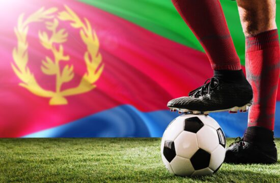 Close up legs of Eritrea football team player in red socks, shoes on soccer ball at the free kick or penalty spot playing on grass.