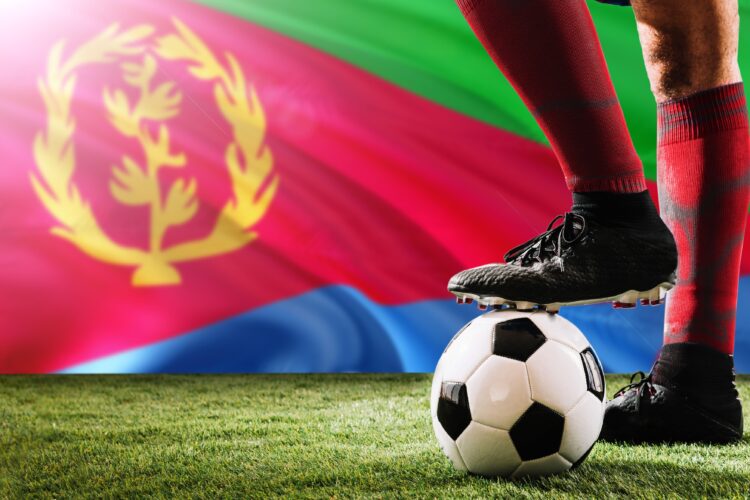 Close up legs of Eritrea football team player in red socks, shoes on soccer ball at the free kick or penalty spot playing on grass.