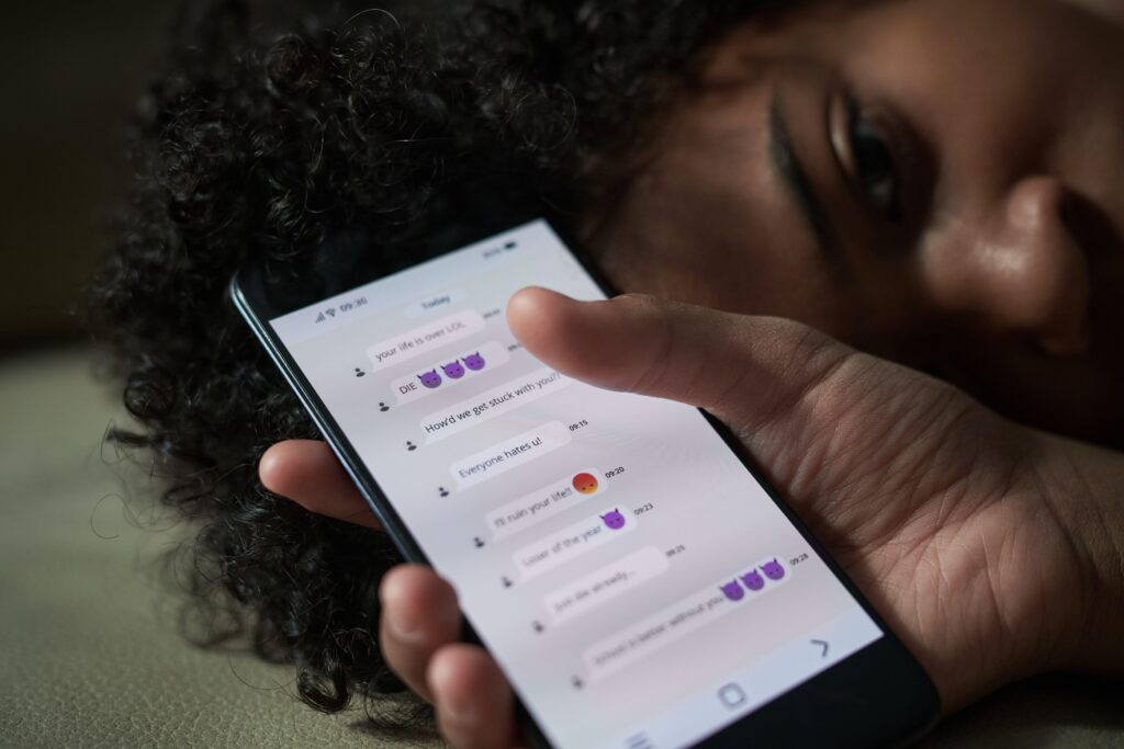 Close up shot of stressed African American teenage boy getting messages from haters on mobile phone indoors